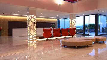 A modern lobby with a reception desk, red chairs, and a seating area with ottomans.