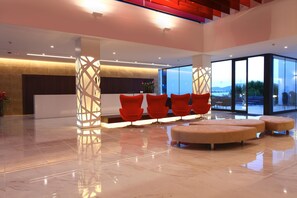 A modern lobby with a reception desk, red chairs, and a seating area with ottomans. - Iberostar Waves Cala Millor (Sant Llorenc des Cardassar)