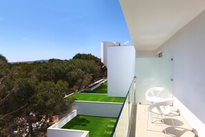 Un bâtiment moderne doté d’un balcon en verre donnant sur une pelouse verdoyante et des arbres.