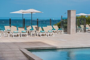 Zona junto a la piscina con sillones de descanso y sombrillas, con vista a una masa de agua.