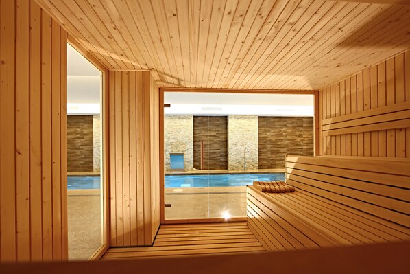 Un sauna en bois, avec un banc, un mur en pierre et une vue sur une piscine extérieure.