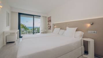 A modern hotel room with a large bed, a desk, and a chair. There is a large window with a view of the sea.