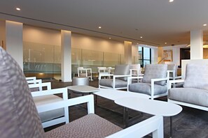 Un espace de détente moderne, avec des meubles blancs, des cloisons en verre et un escalier en arrière-plan.