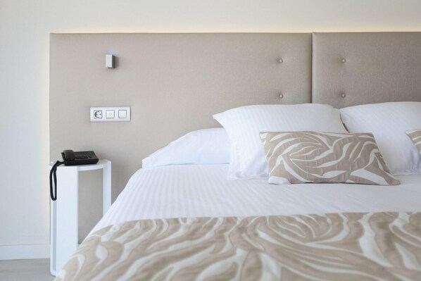 Un lit bien fait, recouvert d’un couvre-lit à motifs, un téléphone sur la table de chevet et un interrupteur fixé au mur.