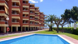 A swimming pool with a lifebuoy, surrounded by a building with multiple balconies and a grassy area with trees. - Rentalmar Sol de España (Cambrils)