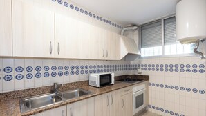 A kitchen with light wood cabinets, a stainless steel sink, a microwave, and a stove. - Rentalmar Sol de España (Cambrils)