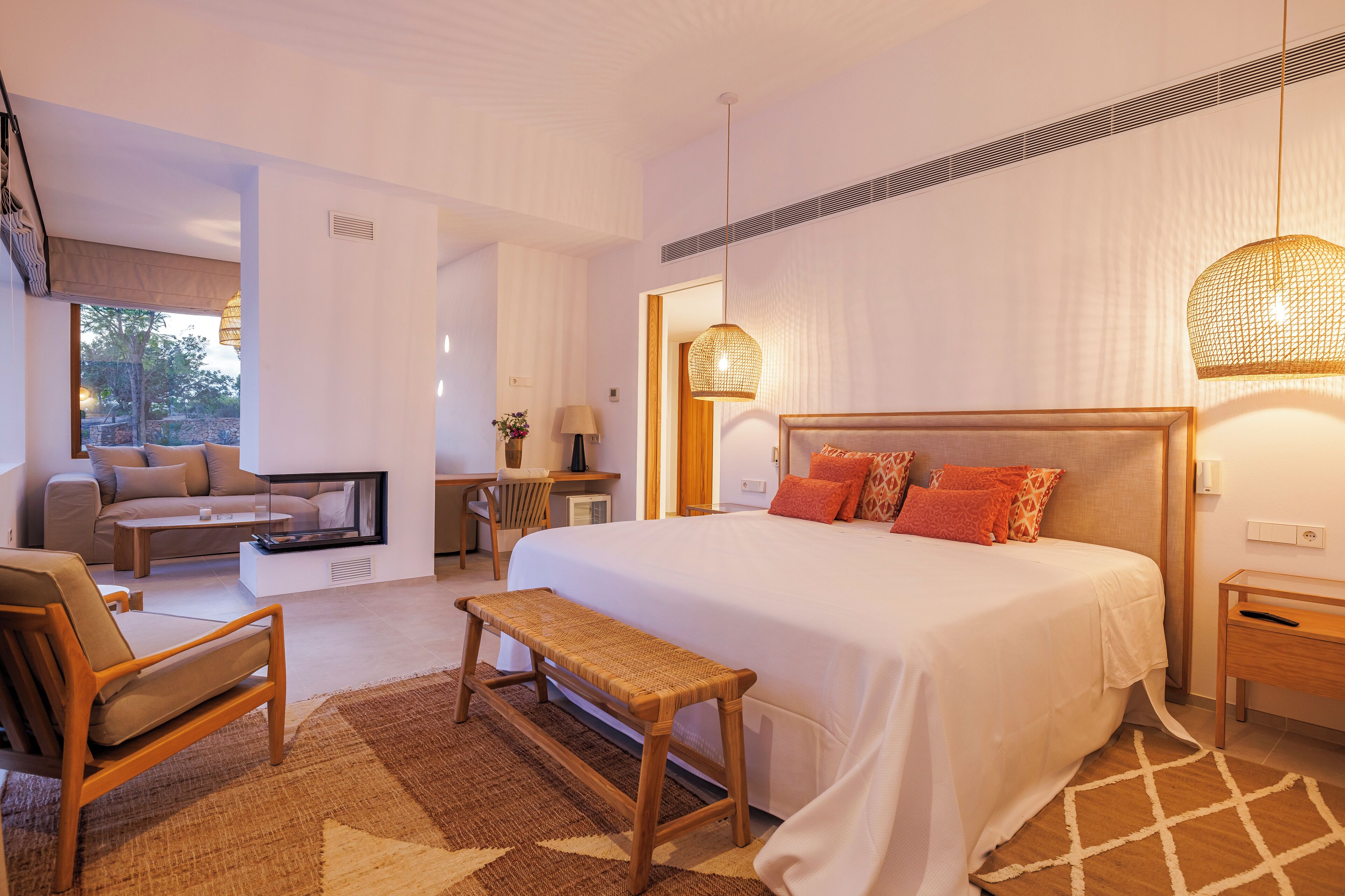 Una camera d'hotel moderna con un letto grande, una zona salotto con divano e poltrona, una scrivania e un'ampia finestra.