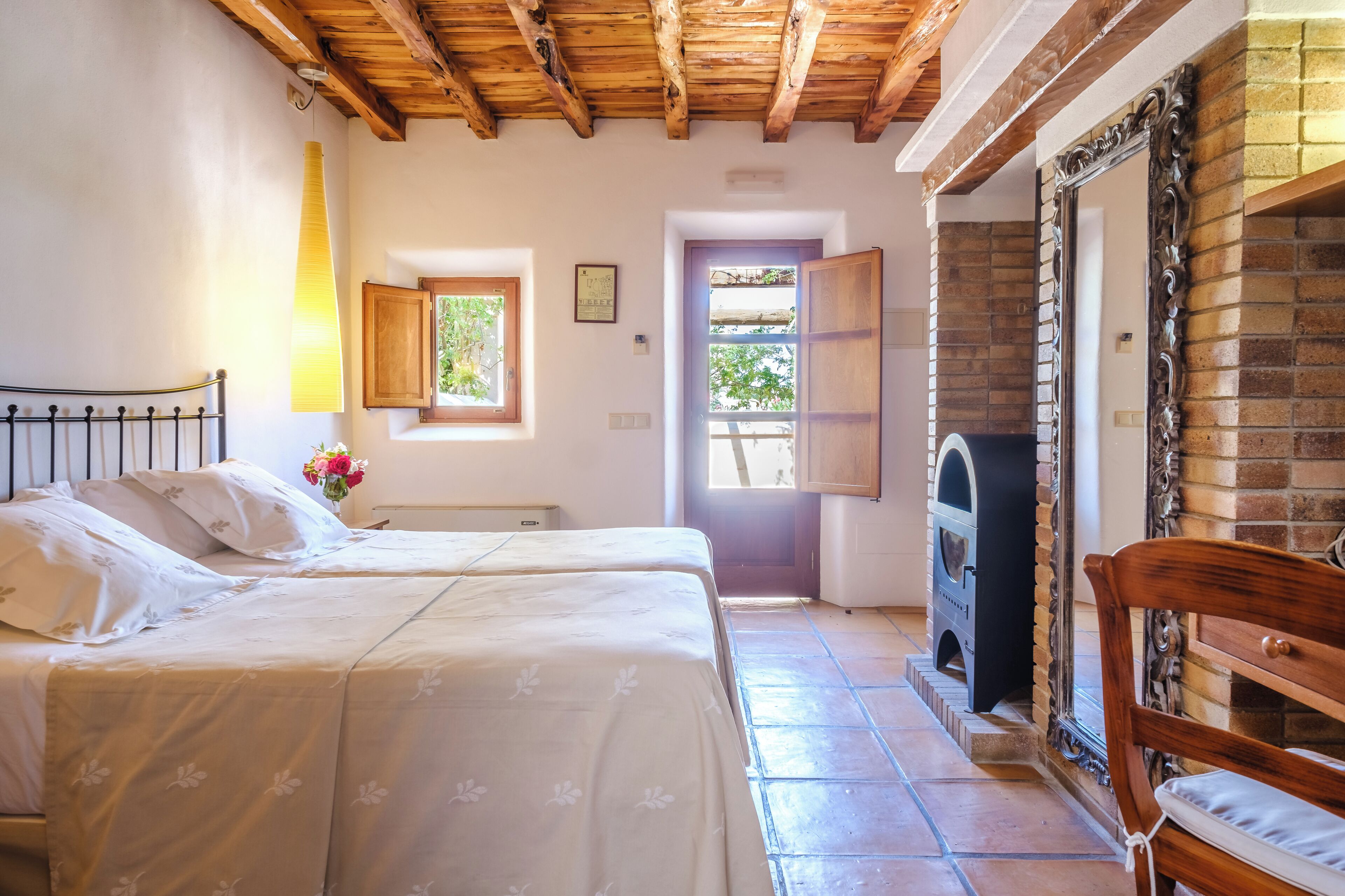 Una camera da letto con due letti, soffitto in legno, camino e finestra vista.