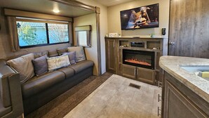 Un intérieur de camping-car chaleureux et confortable, avec un canapé, une cheminée, un téléviseur et une fenêtre offrant une belle vue.