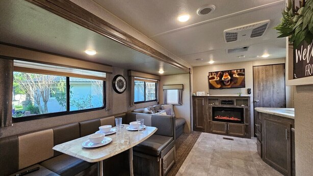 Un intérieur de camping-car compact comprenant un coin repas, des sièges, un coin cuisine et un téléviseur.