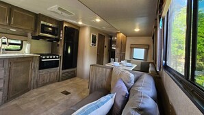 Un intérieur de camping-car compact comprenant un coin cuisine, un espace salon et une fenêtre offrant une vue sur la verdure.