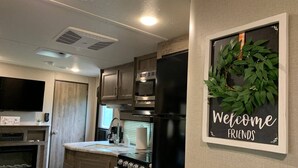 Une cuisine compacte avec des meubles en bois, un four encastré, un réfrigérateur et une enseigne fixée au mur sur laquelle on peut lire : « Bienvenue, amis ».