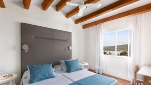 A double bed with blue bedding, a ceiling fan, and a view of the landscape through a window. - TRH Tirant Playa (Mercadal)