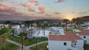 A coastal resort with a central pool, palm trees, and white buildings with red-tiled roofs. - TRH Tirant Playa (Mercadal)