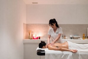 Sesión de masoterapia en un spa, con un cliente acostado en una camilla de tratamiento, un terapeuta atendiendo al cliente y diversas comodidades de spa al fondo.