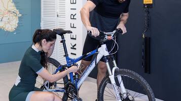 A man and a woman adjusting a bicycle in a room with a map on the wall and a sign that reads "LIKE FRIENDLY".