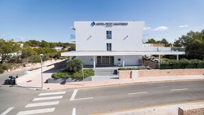 Un hotel moderno con techo plano, acceso cubierto y una zona ajardinada con escalones hacia la entrada.