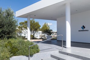 A modern building with a white exterior, a logo on the wall, and a staircase leading to an upper level. - Petit Sagitario (Ciutadella de Menorca)