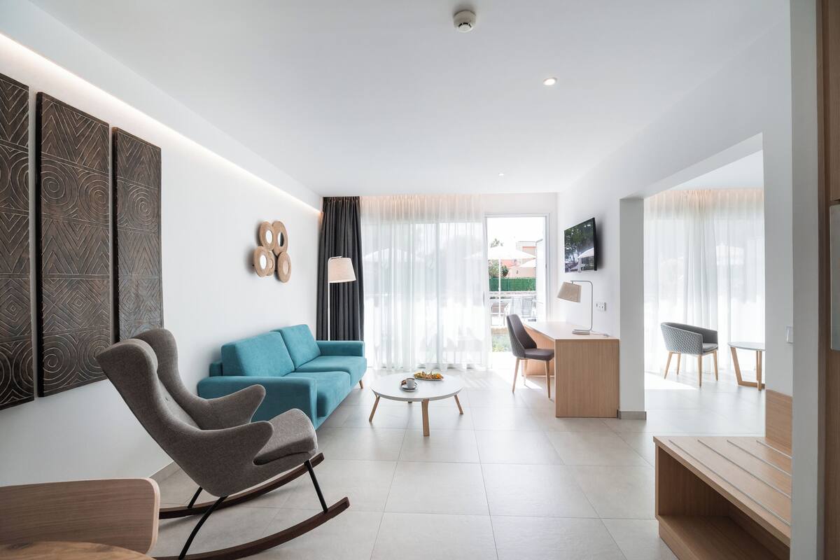 Una sala de estar moderna con un sofá azul, un sillón mecedora, una mesa de centro y un televisor montado en la pared.