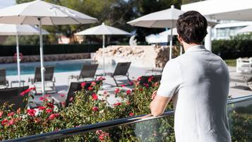 Un hombre de pie junto a una piscina con sillones de descanso y sombrillas.