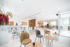 Un moderno vestíbulo de hotel con mostrador de recepción, zona de estar y ventanas amplias.