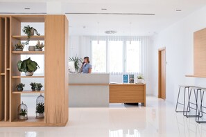 Een moderne receptiebalie met een houten bureau, een plantenrek en een groot raam.