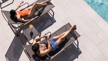 Two sun loungers by a poolside with clear water.