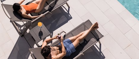 Two sun loungers by a poolside with clear water.