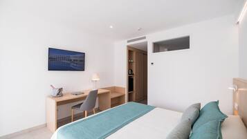 A modern hotel room with a bed, a desk, and a chair. There is a painting on the wall and a small window.