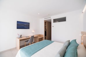 Una habitación de hotel moderna con una cama, un escritorio y una silla. Hay un cuadro en la pared y una ventana pequeña.