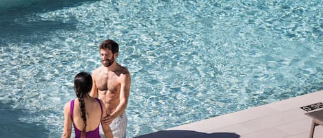 Ein Paar an einem Pool mit klarem Wasser, einer gefliesten Terrasse und einem Tisch am Pool.