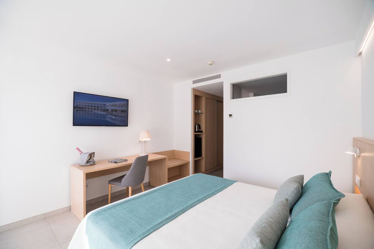 Una habitación de hotel moderna con una cama, un escritorio y una silla. Hay un cuadro en la pared y una ventana pequeña.