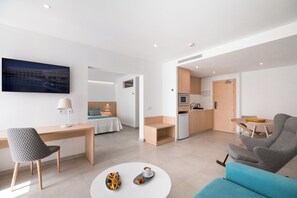 Habitación de hotel moderna con cama, escritorio, kitchenette y sala de estar con sofá y mesa de centro.
