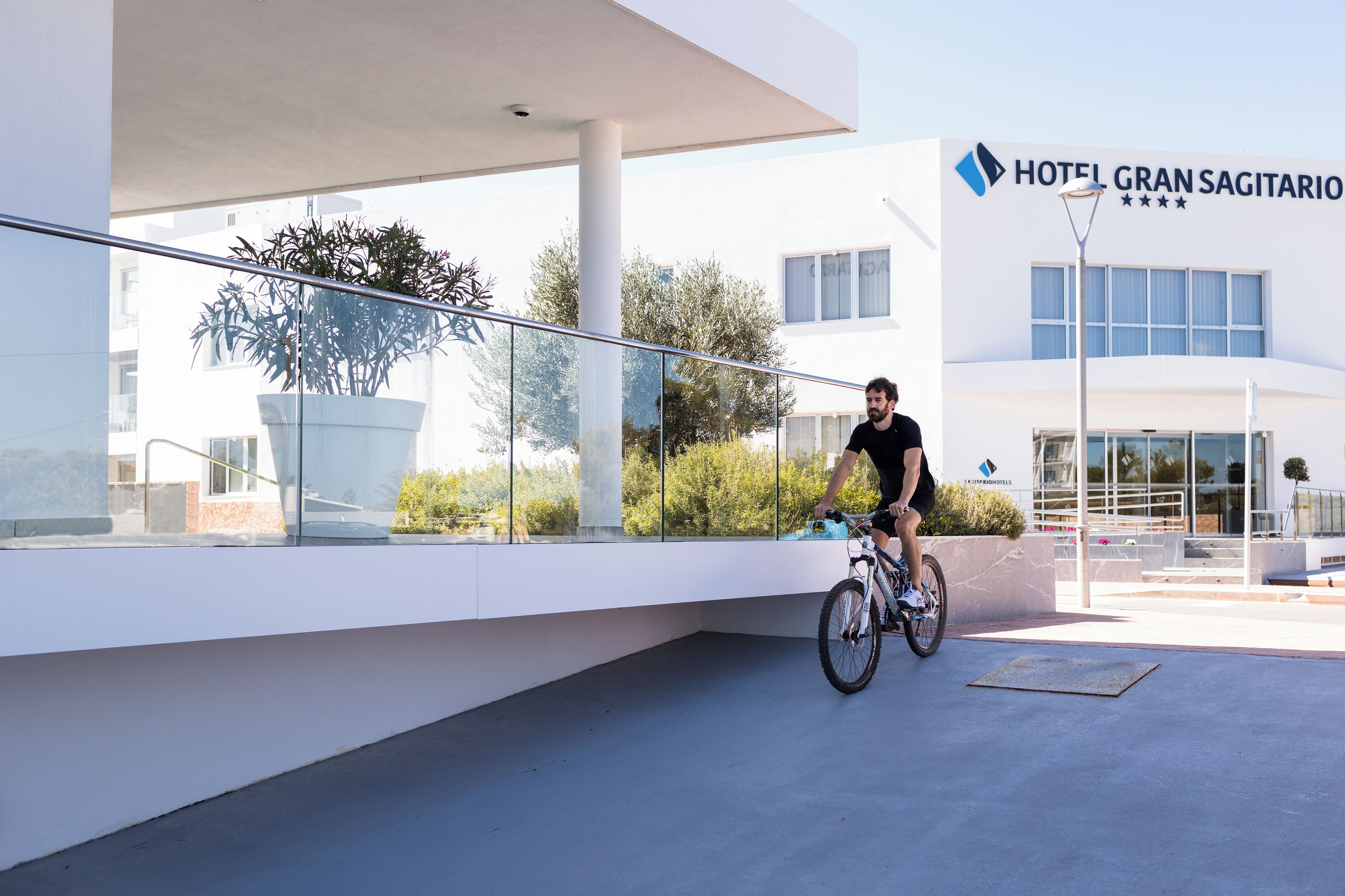 A modern hotel building with a glass facade, a cyclist on the ground, and a clear sky.