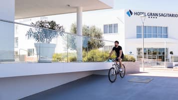 A modern hotel building with a glass facade, a cyclist on the ground, and a clear sky.