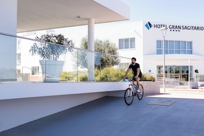 Un moderno edificio de hotel con fachada de vidrio, un ciclista en el suelo y cielo despejado.