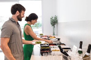 A buffet setup with various food items and a bottle of champagne in a glass container. - Petit Sagitario (Ciutadella de Menorca)