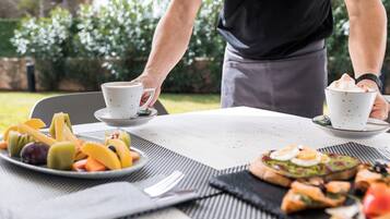 Ein Tisch mit einer Fruchtschale, einer Toastscheibe mit Eiern und zwei weißen Tassen auf Untertellern.