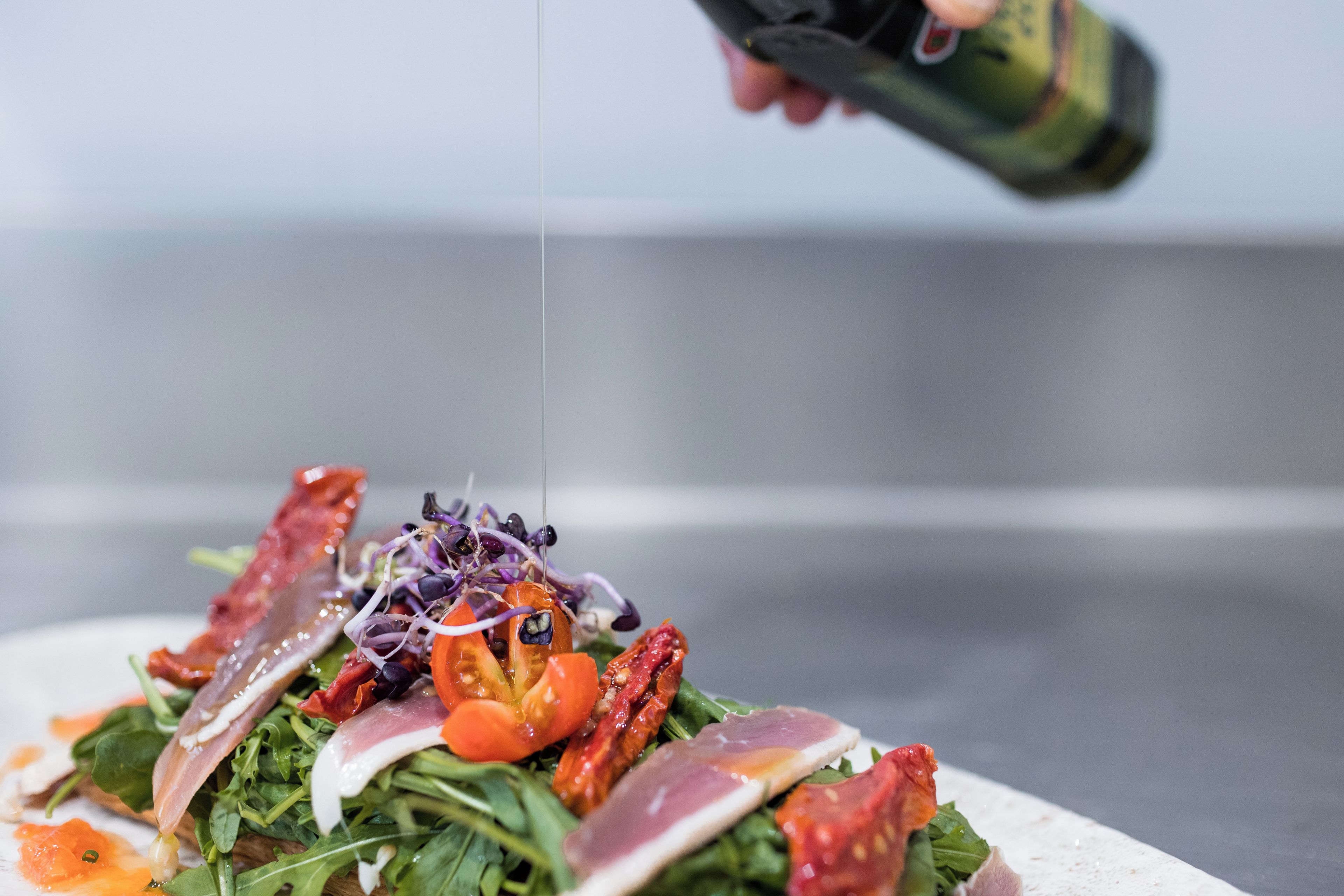 Primer pla d'un plat amb diversos ingredients, com ara verdures, tomàquets i carn, que s'està preparant a la cuina.