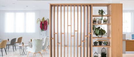 A modern office space with a wooden partition, round tables, and chairs, and shelves with potted plants.