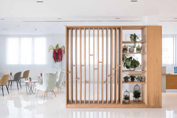 Un espacio de oficina moderno con un separador de madera, mesas redondas, sillas y estanterías con plantas en macetas.