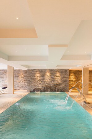 An indoor swimming pool with clear water, stone walls, and modern lighting. - Petit Sagitario (Ciutadella de Menorca)