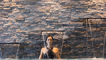 A woman in a pool with water jets against a stone wall.