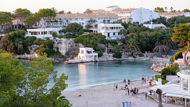 Un hotel frente al mar con varias construcciones, una playa y un litoral rocoso.