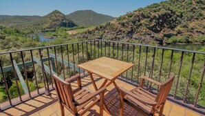 A balcony with a wooden table and two chairs, overlooking a river and hills. - Hotel Rural Aldeaduero (Saucelle)