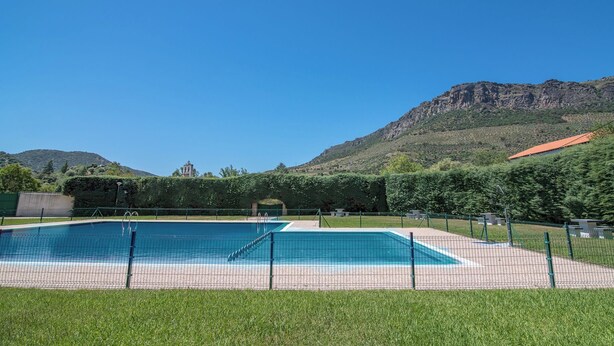 A rectangular swimming pool with a surrounding fence, set against a backdrop of mountains and greenery. - Hotel Rural Aldeaduero (Saucelle)