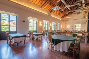Un amplio comedor con numerosas mesas y sillas, ventanas grandes que dejan entrar luz natural y un techo alto con vigas a la vista.