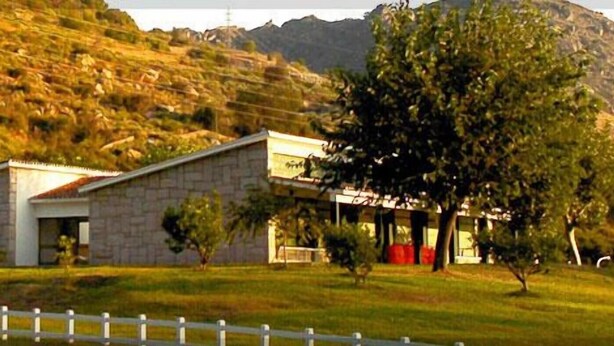 A two-story stone building with a flat roof, surrounded by a white picket fence, set against a hilly backdrop. - Hotel Rural Aldeaduero (Saucelle)