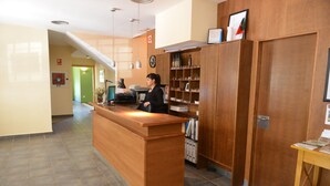 A reception desk with a woman standing behind it, a clock, and a shelf with various items. - Hotel Rural Aldeaduero (Saucelle)