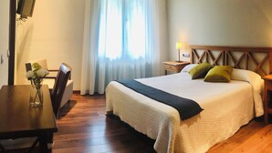 A hotel room with a large bed, a wooden desk, a chair, a TV mounted on the wall, and a window with curtains. - Hotel Rural Aldeaduero (Saucelle)